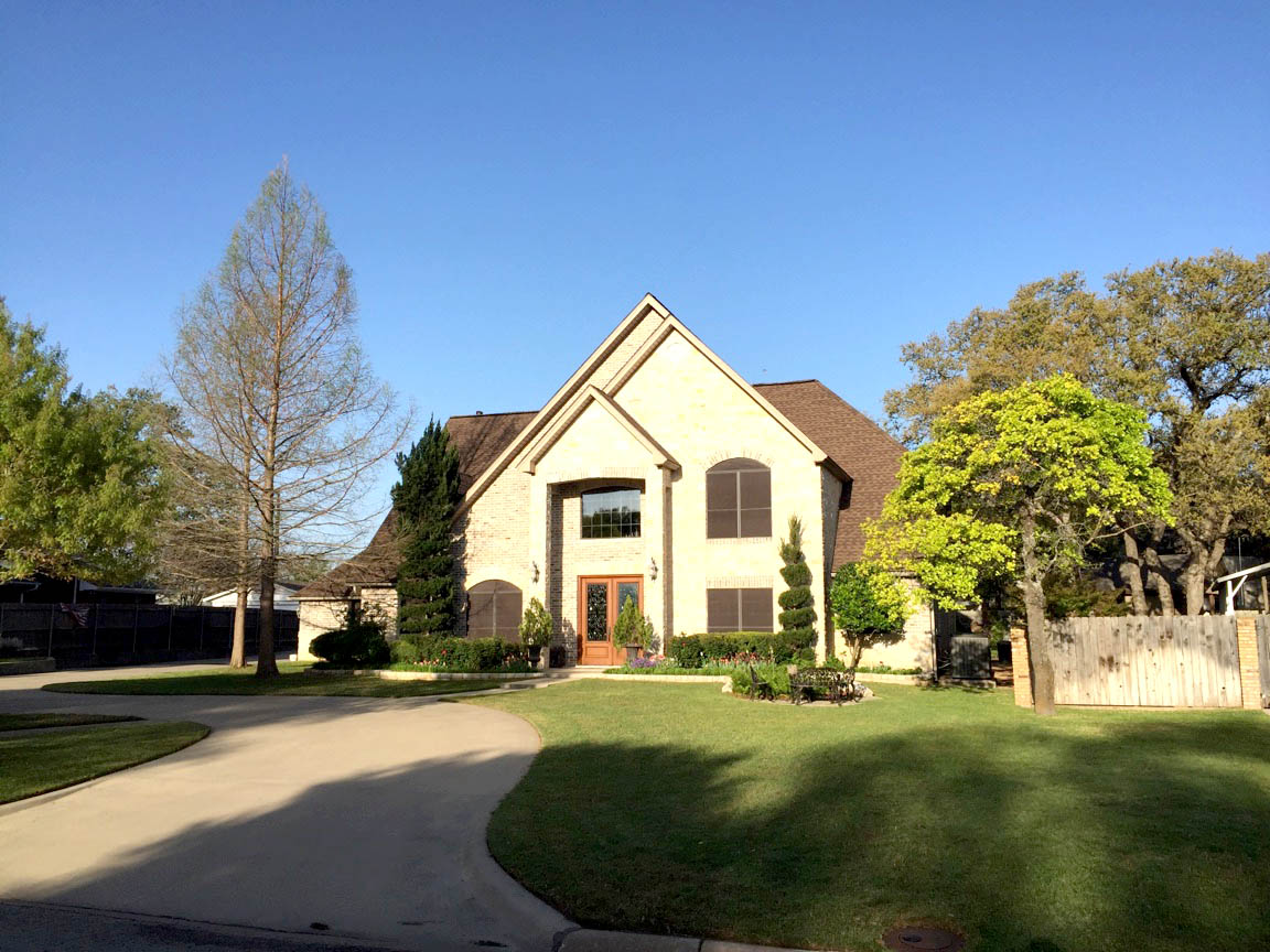 Two-story brick and stone home with new dark brown architectural shingles — Heritage Roofing Stephenville TX