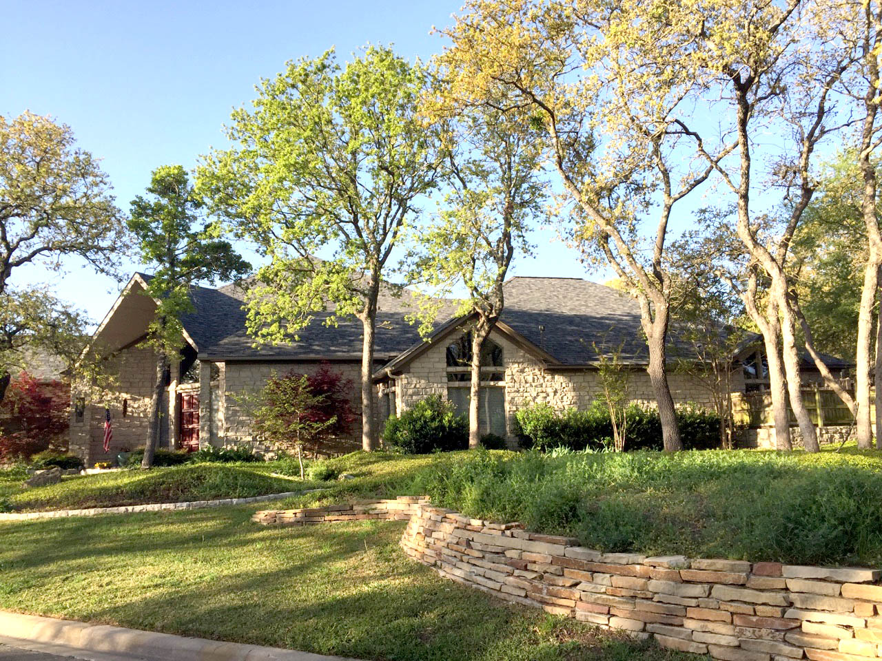 Single-story stone ranch home with new dark gray architectural shingles surrounded by oak trees — Stephenville TX