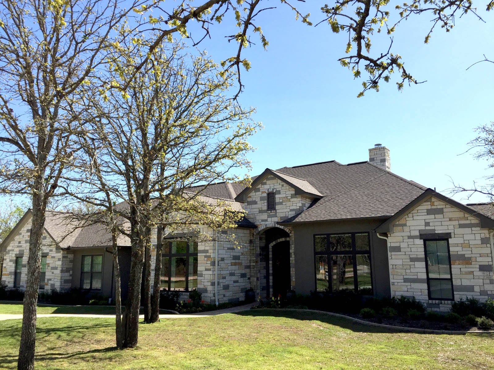 Modern Texas stone home with taupe architectural shingles — Heritage Roofing new construction