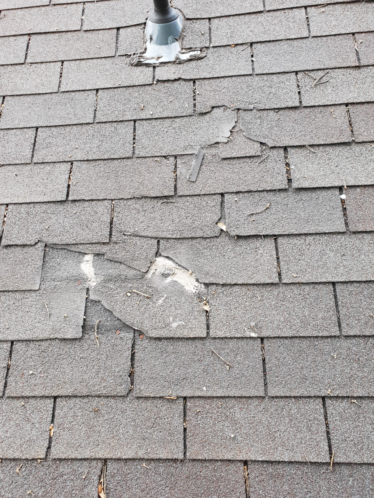 Wind-blown and cracked shingles near pipe boot — storm damage in Central Texas