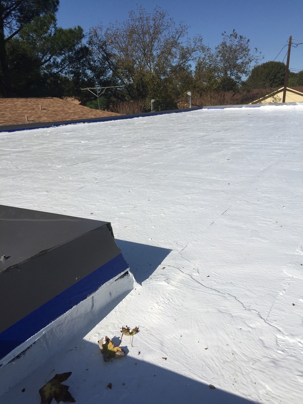 Large white commercial foam/TPO roof with curb-mounted HVAC unit — Heritage Roofing